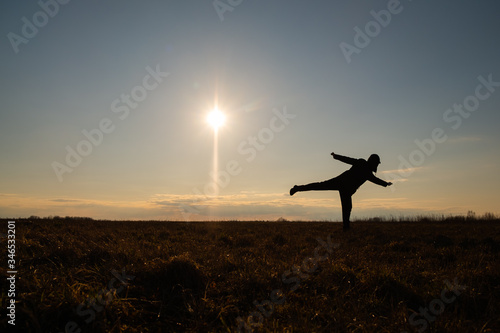 Fototapeta Naklejka Na Ścianę i Meble -  The contour of a man against the sky. The man took a pose in the form of an airplane flying away from the sun. The concept of solitude with nature and tranquility