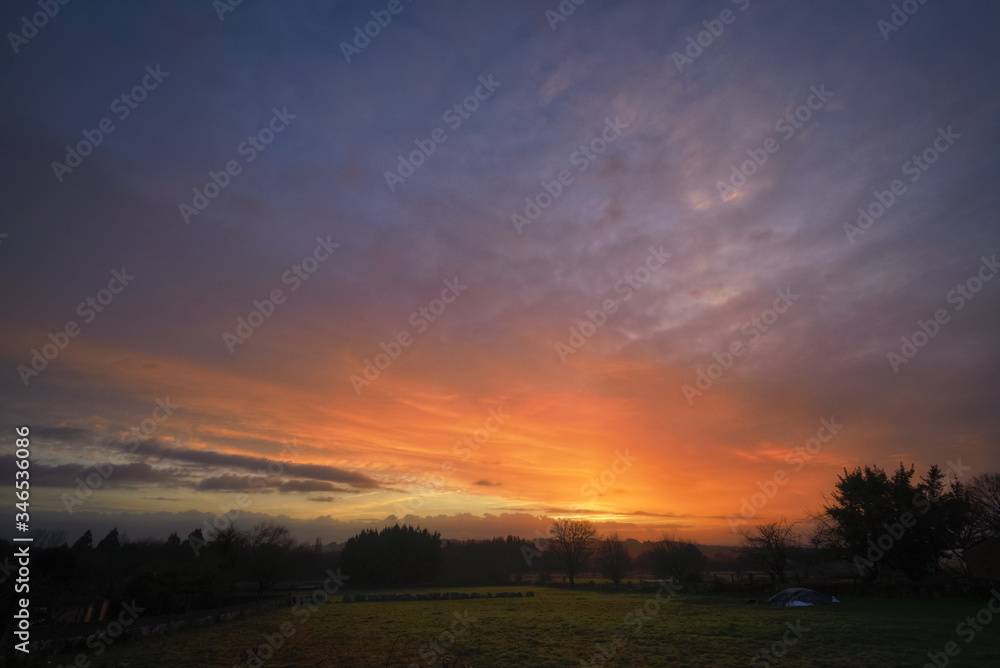 Orange fiery Cloudscape at Sunrise over Pasture land