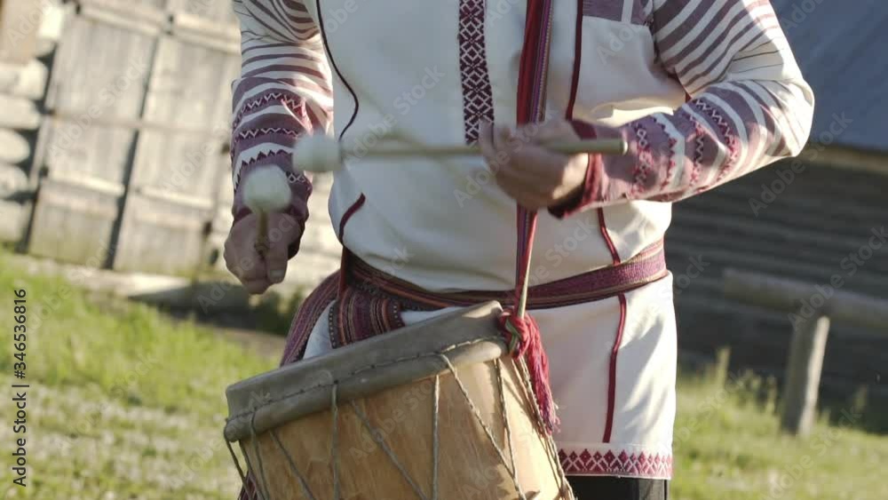 Man in traditional russian clothes dancing and playing on folklore drum