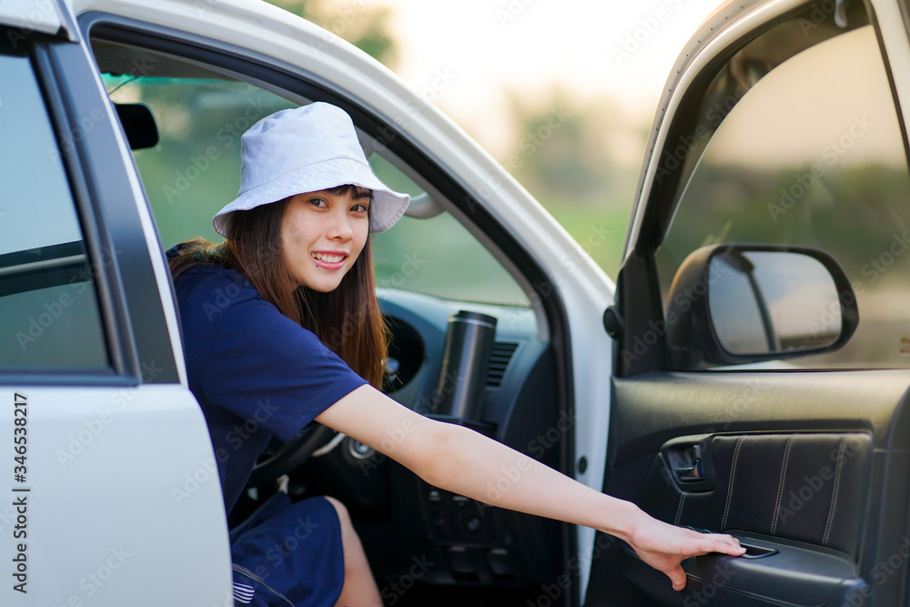 Young beautiful Asian woman wearing white hat sitting at driver position in SUV car and ready to close the door before roadtrip. Holiday travel concept