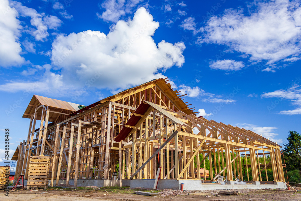Construction of house with wooden frame erected against blue sky Construction of house with wooden frame erected against blue sky