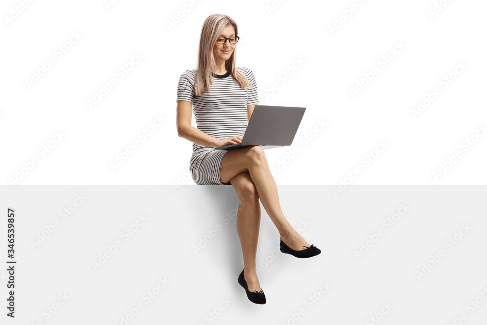 Young woman working on a laptop and sitting on a blank panel Young woman working on a laptop and sitting on a blank panel