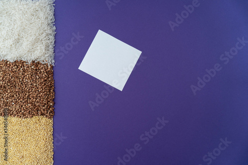 Purple background with white rice, brown fried buchwheat, yellow millet and white paper blank note, donation concept during quarantine, cereal concept, copy space, photo