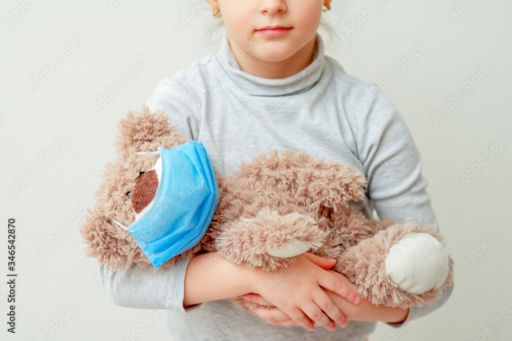 Child is holding a toy bear in a medical mask due epidemic of coronavirus on light background. Health care concept. Child is holding a toy bear in a medical mask due epidemic of coronavirus on light background. Health care concept.