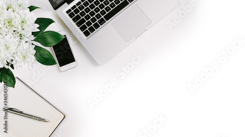 Workspace with laptop, notebook, smartphone, pen and flowers bouquet on white table. Flat lay, top view
