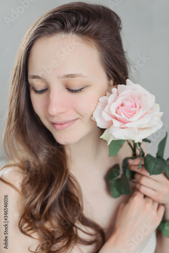 A young brunette girl without makeup holds a pink rose. Flower. Natural beauty.