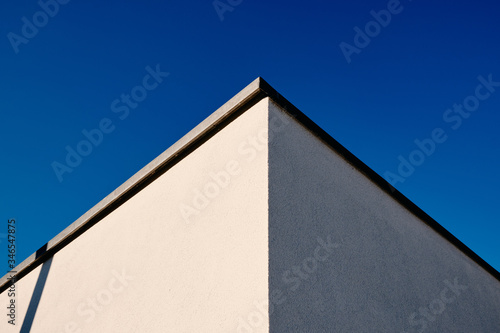 Abstract architecture shot of two walls and a corner of a modern house with white plaster against clear blue sky. Seen in Germany in March.