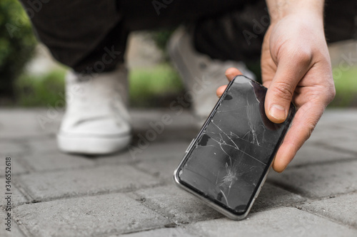 Man hand take broken damaged smartphone from asphalt