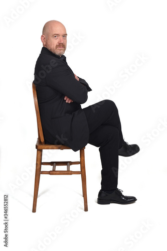 portrait of a man sitting on a chair side view and looking at camera on white background,