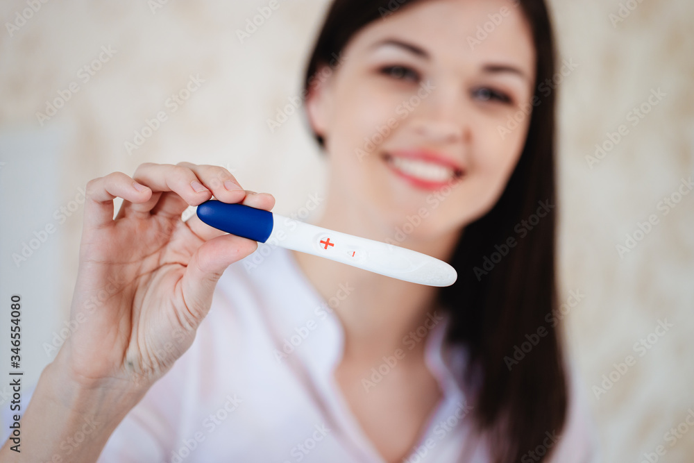 Young woman rejoices while looking at a positive pregnancy test Young woman rejoices while looking at a positive pregnancy test