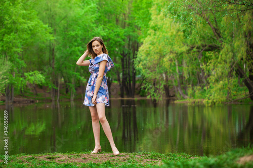 Portrait of a young beautiful woman in blue dress posing by the lake