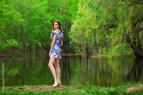 Portrait of a young beautiful woman in blue dress posing by the lake