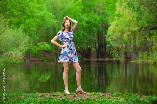 Portrait of a young beautiful woman in blue dress posing by the lake