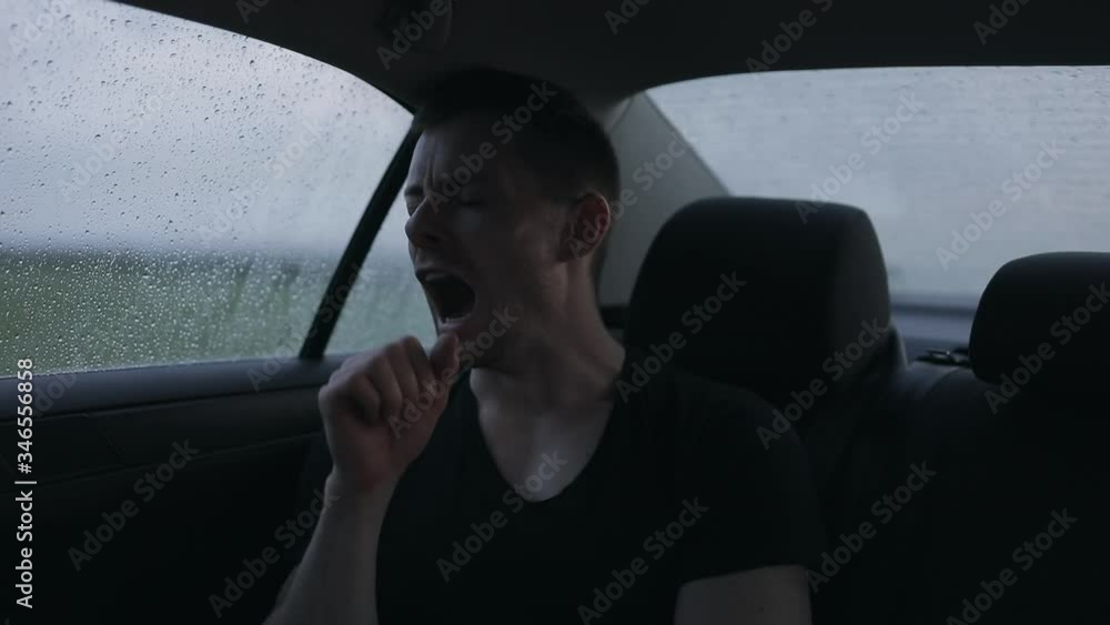 Sleepy man yawns in a car at the rainy day Sleepy man yawns in a car at the rainy day