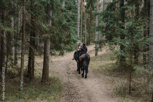 2 people ride a black horse in the forest