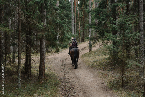 2 people ride a black horse in the forest