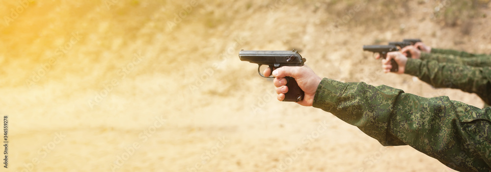 A military man in uniform, a man s hand with a gun aiming for firing a firearm. Shooting practice at a shooting range or pitch training ground and dash. Police, army and border police training.