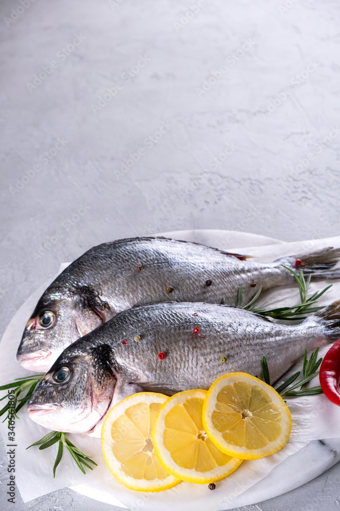 Delicious fresh fish on gray background. Fish with aromatic herbs, spices and lemon - healthy food, diet or cooking concept Delicious fresh fish on gray background. Fish with aromatic herbs, spices and lemon - healthy food, diet or cooking concept