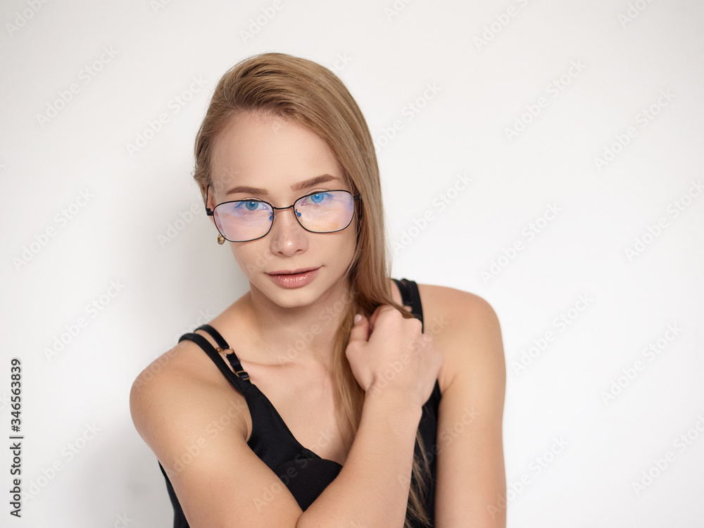 Headshot portrait of a cute natural looking blonde woman wearing simple black blouse and nerd glasses posing on a white background touching her shoulder Headshot portrait of a cute natural looking blonde woman wearing simple black blouse and nerd glasses posing on a white background touching her shoulder