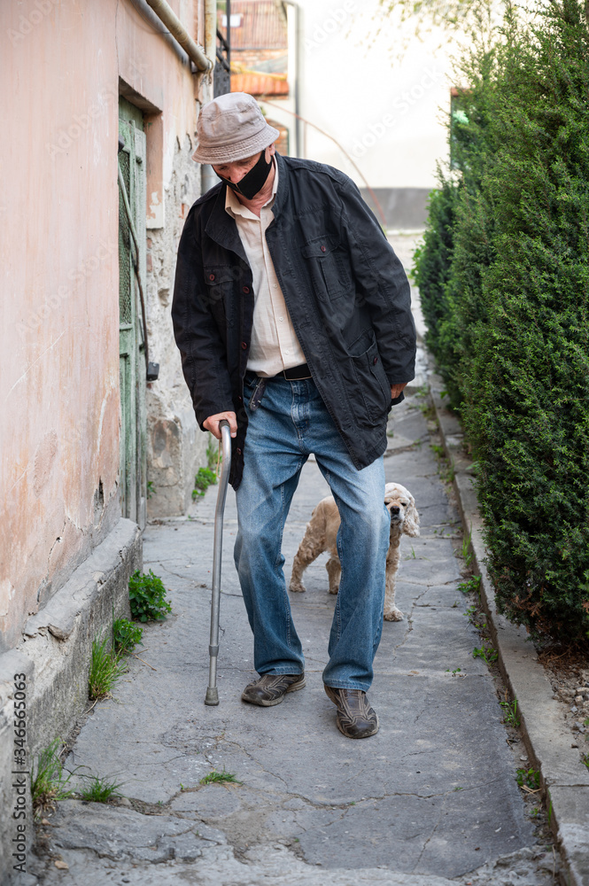 Man in protective mask with a cane walking with a dog