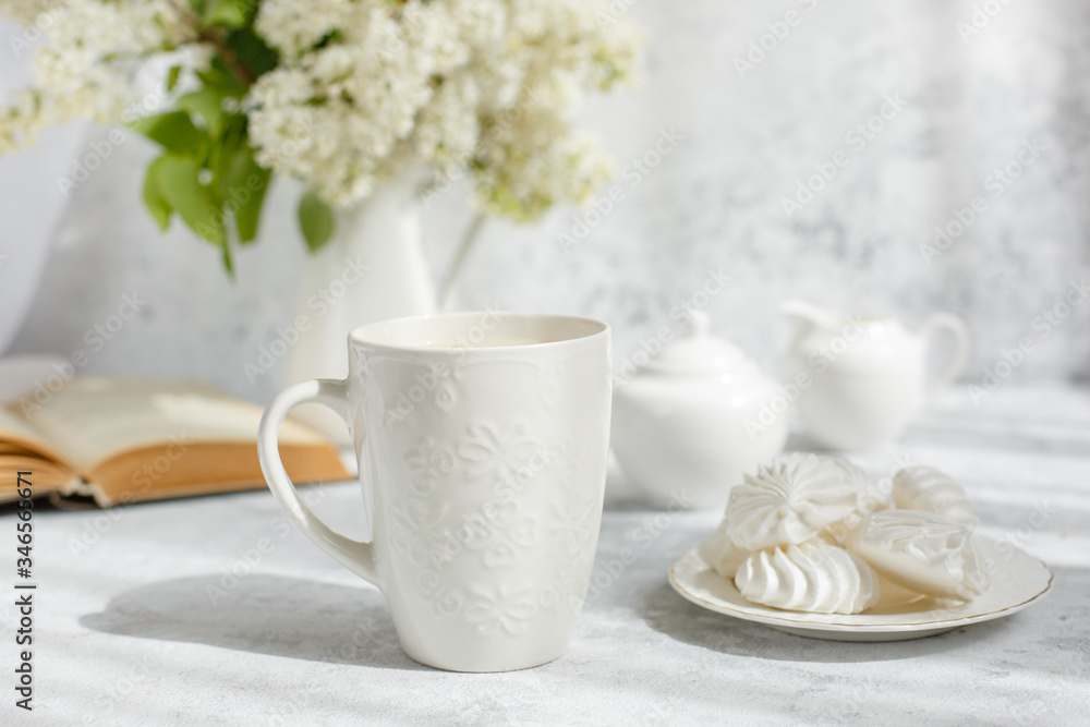 Still life vase with a bouquet of white lilac, a Cup of coffee with marshmallows, a plate of meringue, a sugar bowl and a milk jug , an old book. Postcard good morning. Still life vase with a bouquet of white lilac, a Cup of coffee with marshmallows, a plate of meringue, a sugar bowl and a milk jug , an old book. Postcard good morning.