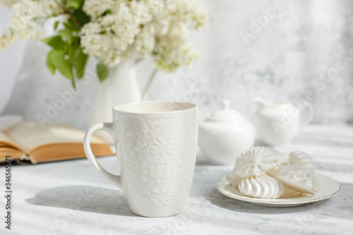 Still life vase with a bouquet of white lilac, a Cup of coffee with marshmallows, a plate of meringue, a sugar bowl and a milk jug , an old book. Postcard good morning.