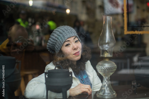 Asian woman posing for a photographer reflection in the glass  looks out from behind the cafeteria window.