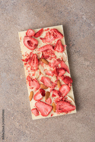 A bar of white chocolate with fried almonds and freeze-dried strawberries on a light background. Top view, flat lay.