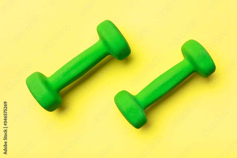 two green dumbbells on a yellow background two green dumbbells on a yellow background