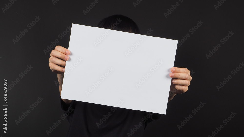 female model's hands is holding the A4 paper on black background. female model's hands is holding the A4 paper on black background.