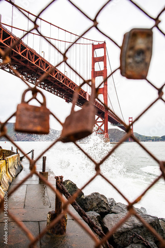 The Golden Gate Bridge behind a fence line with rusted  locks hanging on it. 
