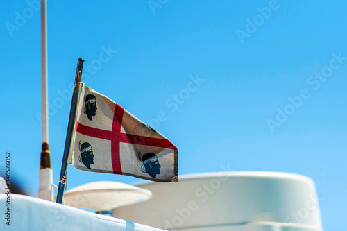 A view of a Sardinian flag blowing in the wind on top of a yacht with the blue sky in the background on a sunny day, in Sardinia Italy