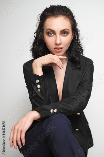 A beautiful young girl with wet curly hair in trousers and a black jacket on a bar chair.