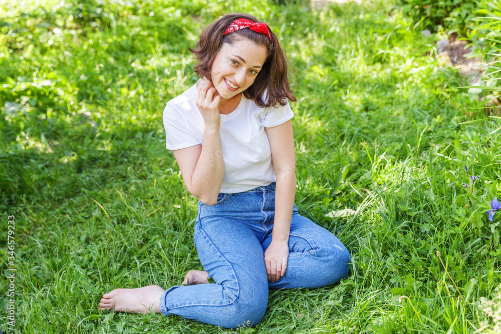 Fototapeta premium Happy girl smiling outdoor. Beautiful young brunete woman with brown hair resting on park or garden green grass background. European woman. Positive human emotion facial expression body language