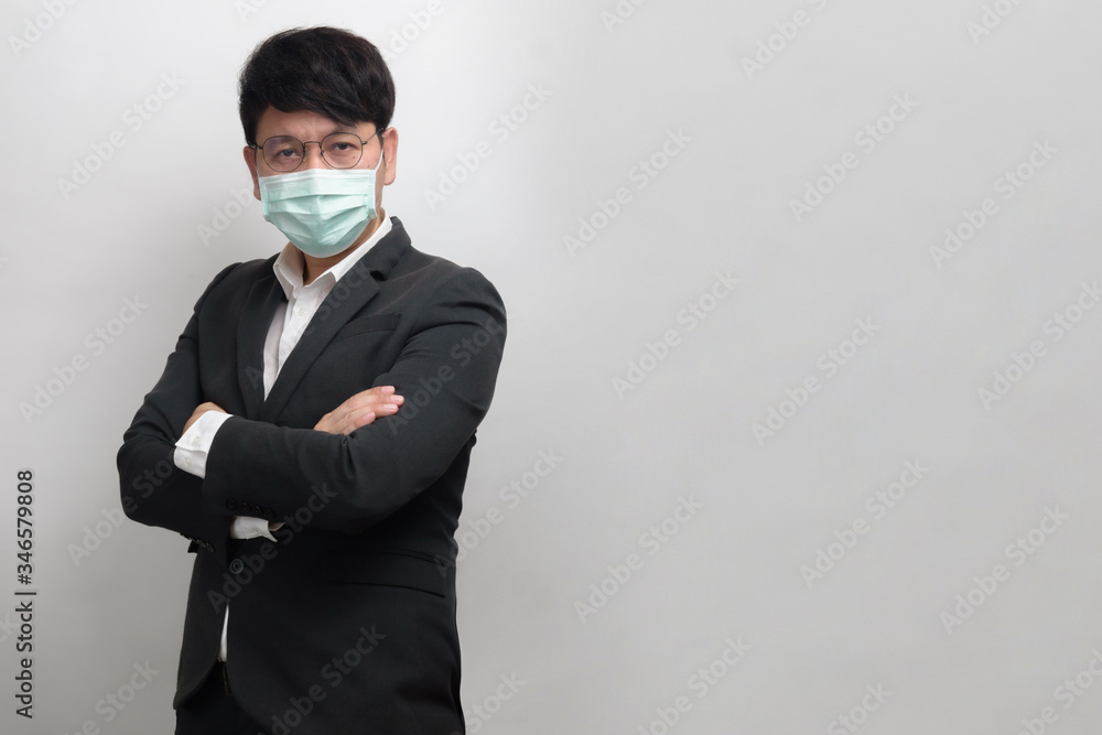 Asian businessman wearing surgical face mask in formal black suit jacket, crossing the arms, look at the camera, studio lighting isolate with grey background, concept for coronavirus, covid19