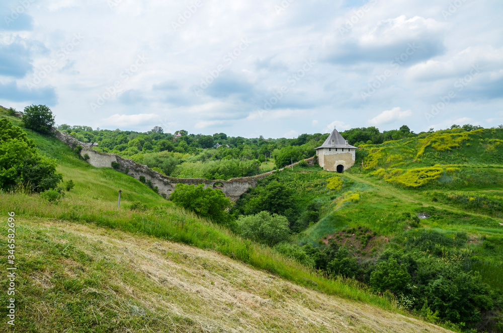 Naklejka premium View of green hills and ruined walls on one of the entry gates of Khotyn Fortress on Dniester riverside in Ukraine. Traveling concept background