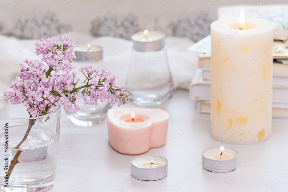 Pastel room interior decor with burning hand-made candle, books, flowers. Cozy and relax concept.