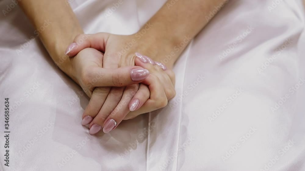 CU, slow motion: elegant young woman holds gentle hands with beautiful pink manicure with glitter dots on white skirt fabric in light room close view CU, slow motion: elegant young woman holds gentle hands with beautiful pink manicure with glitter dots on white skirt fabric in light room close view