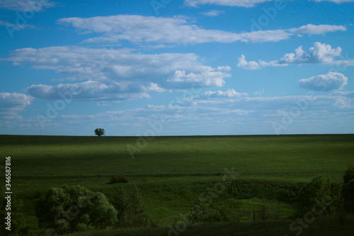 minimalistic summer landscape with a green field and blue sky with clouds