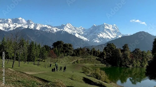 Snow covered mountains surrounded by forest & clear blue skies perfectly reflected in lake on a clear morning. Amazing Himalaya landscape during spring trek to Deoria lake, Chopta, Uttarakhand (India) photo