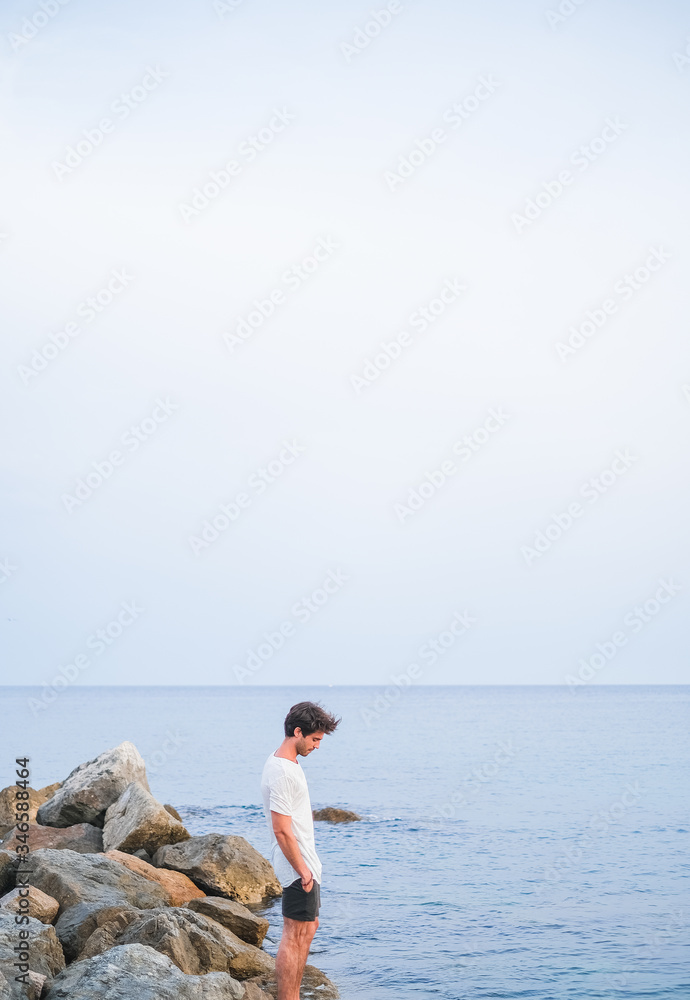 Young caucasian man with his hands in his pockets on a stone pier in the sea