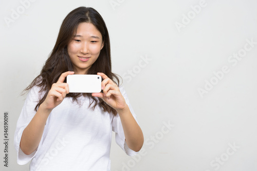 Portrait of happy young beautiful Asian woman taking picture with phone