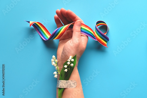 Thank you doctors and nurses! Rainbow ribbon in hand of mature woman with chamomile flower and grass bouquet attached with medical aid patch. Creative modern flat lay, top view on blue background. photo