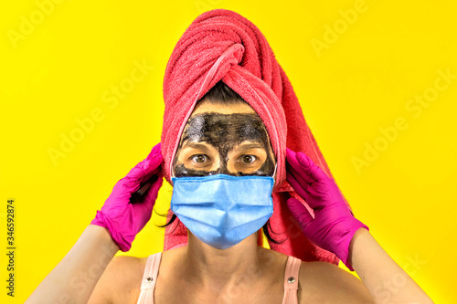 A young beautiful woman with a face mask made of healing black mud and a protective medical mask against the virus. Women's care and self-care in quarantine. Be home. CAVID 2019. photo