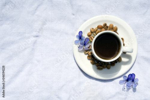 Flat lay Coffee composition with white cup and beans of coffe and blue flower on linen tableclothtable