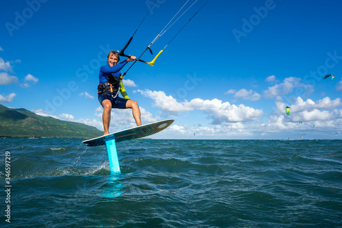professional kiter t rides by hydrofoil on a beautiful background of mountain, spray and beautiful clouds of Mauritius