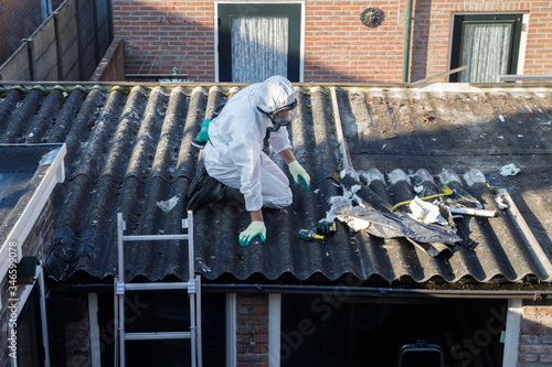 Professional asbestos removal. Man in protective suite removes asbestos roofing.