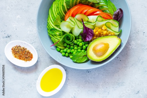 Healthy vegetarian food. Fresh vegetables cucumber, tomato, corn, green peas, avocado, lettuce in a bowl on a blue background. Healthy eating concept.
