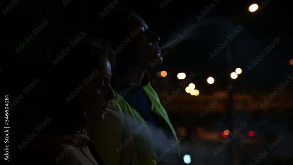 Two girlfriends smoke on the background of the night city. Women smoke cigarettes and vape late at night. Bad habit. Two girlfriends smoke on the background of the night city. Women smoke cigarettes and vape late at night. Bad habit.