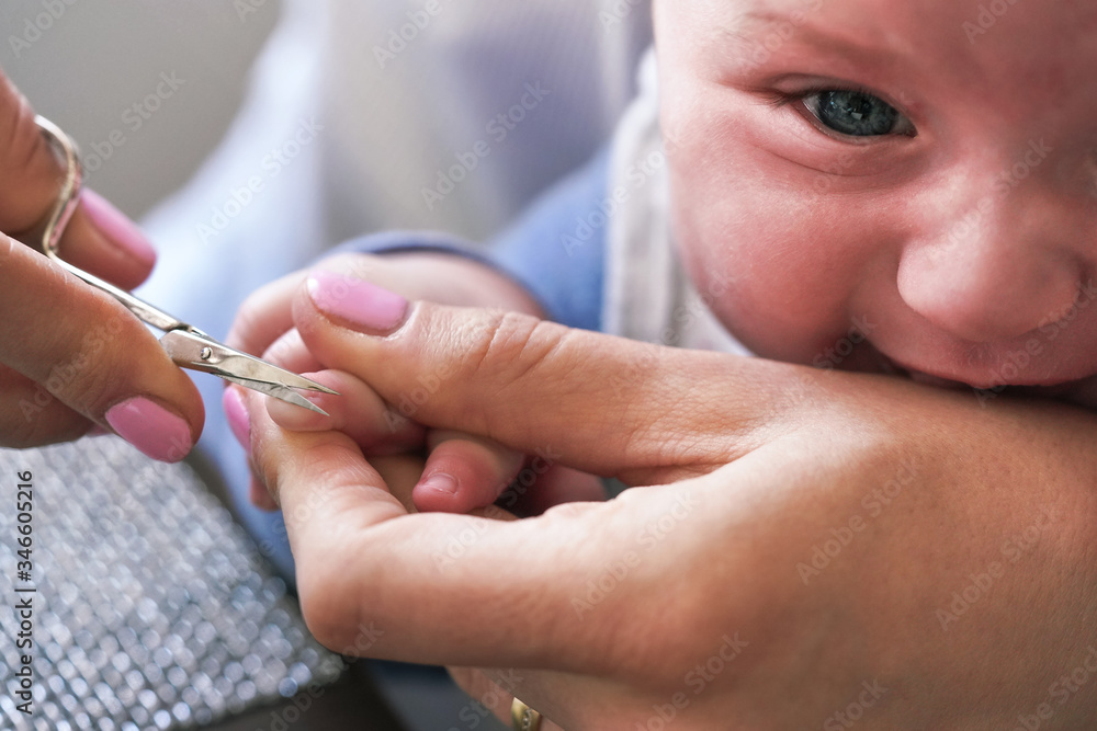 Infant baby boy having his nails cut by mother, detail on scissors and fingertips